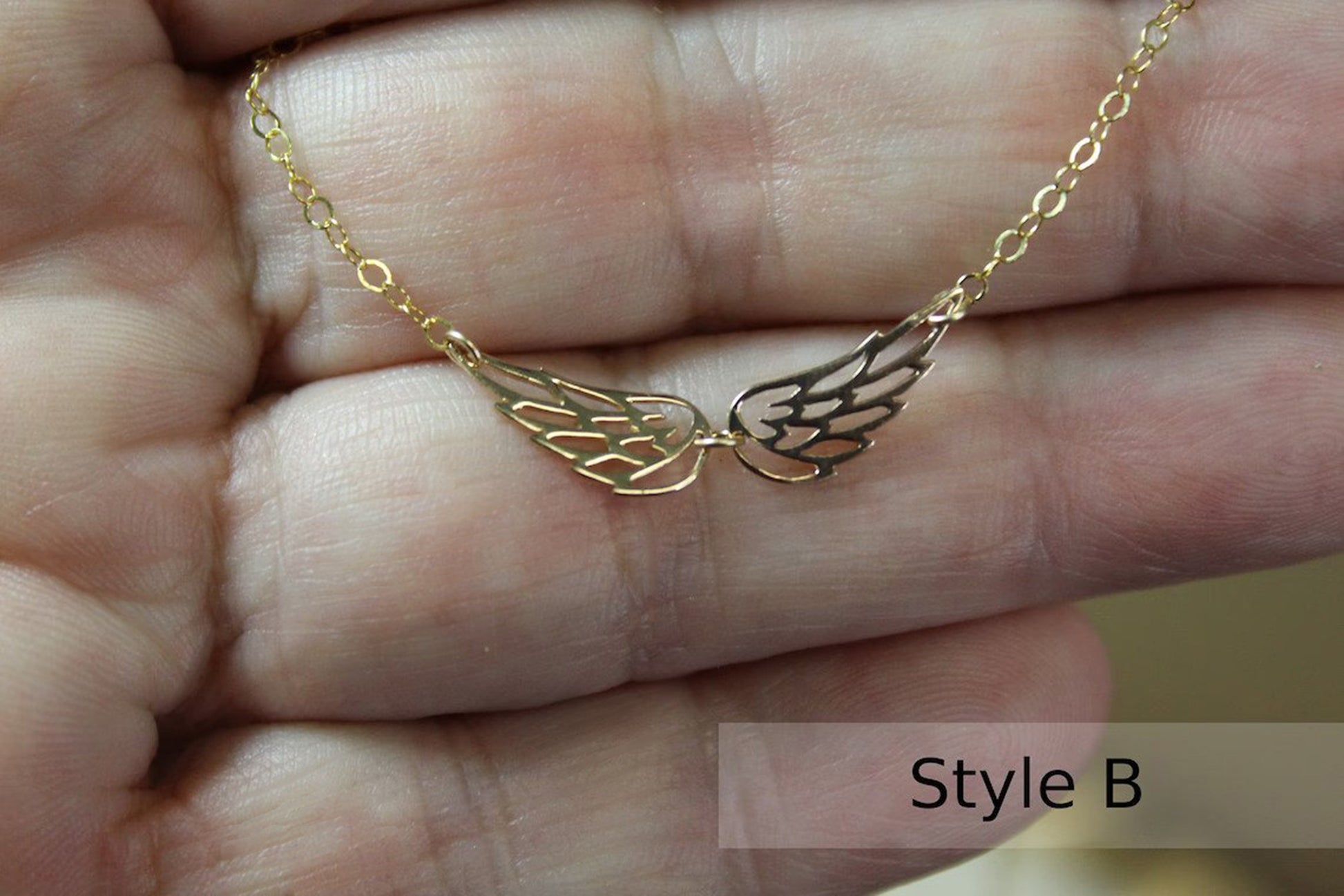 Gold Filled memorial necklace with double angel wing charm is held in a woman's hand.