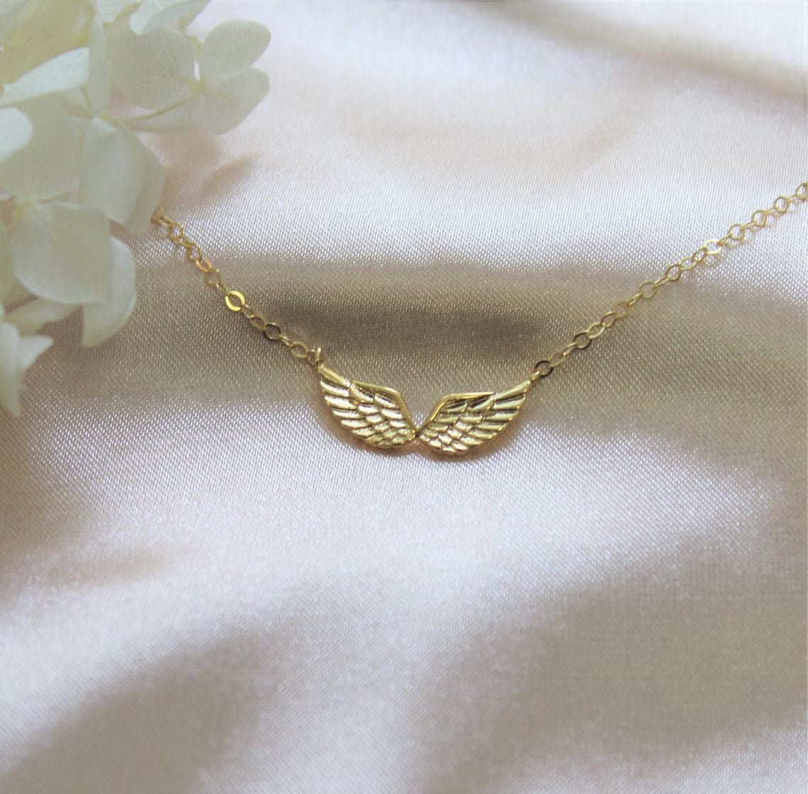Double angel wing necklace charm for memorial gift is laying on a plain white fabric surface.