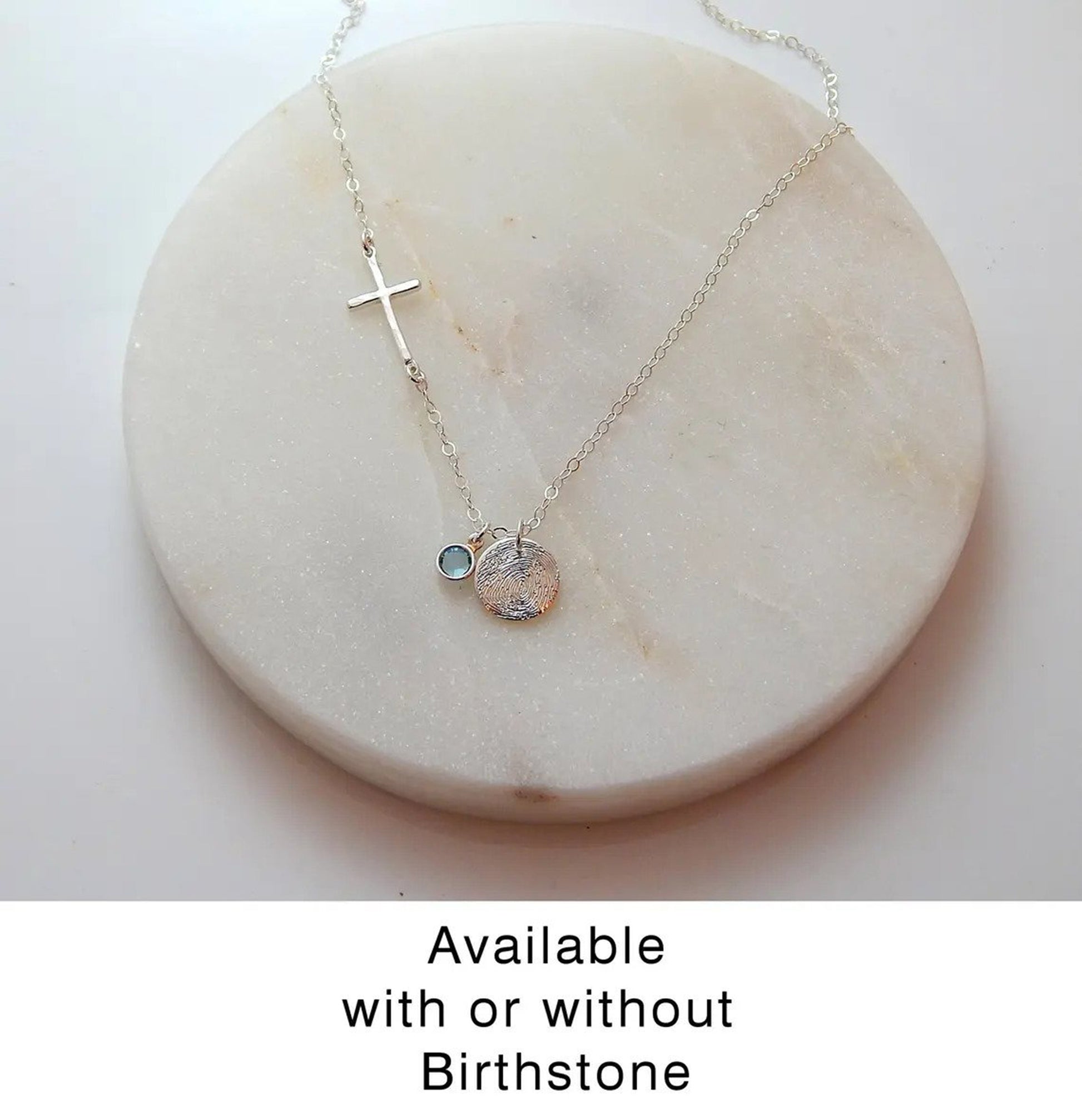 Custom fingerprint necklace with sideways cross and birthstone lays on a marble background.
