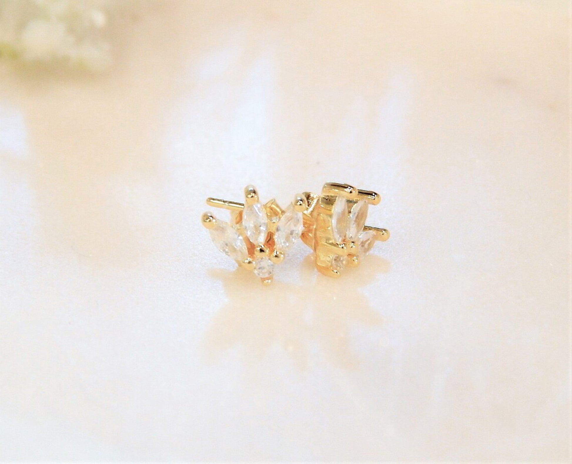 Pair of gold earrings with 4 diamond cubic zirconias are placed on a light and slightly reflective surface.
