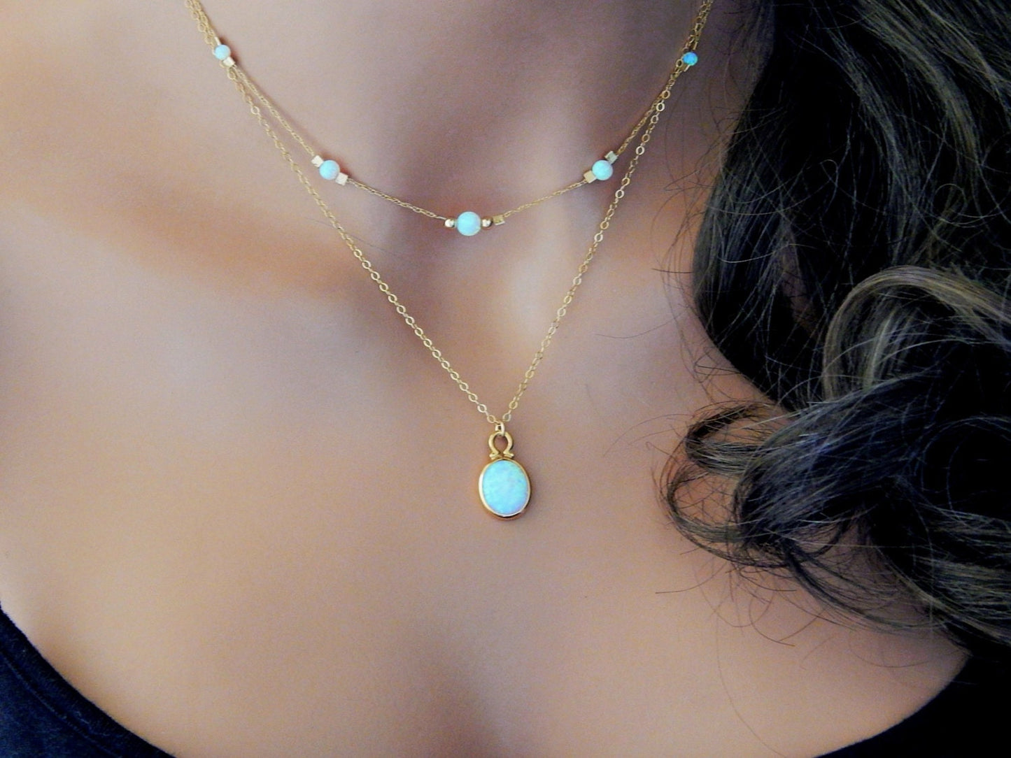 Two handcrafted opal and gold necklaces layered together worn on a model's neck.
