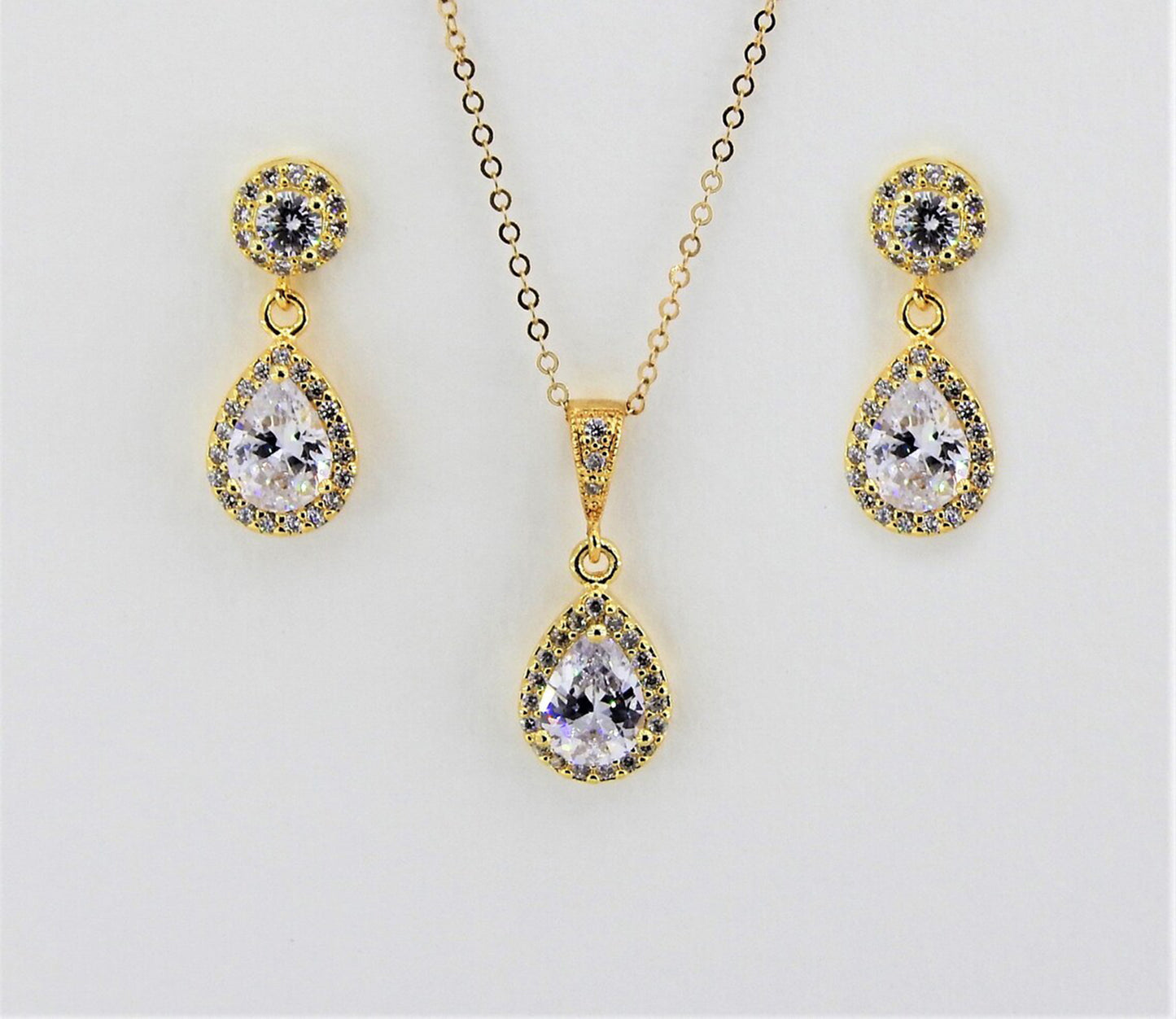 Gold filled earring and necklace set with teardrop diamond surrounded by many tiny cubic zirconias are displayed against a plain white background.