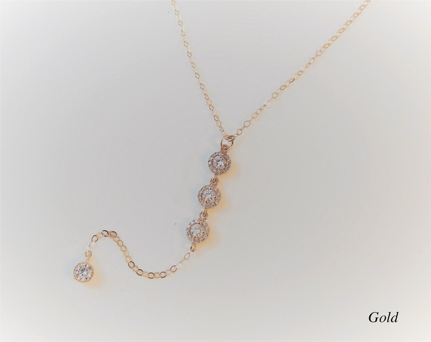 Gold filled bridesmaid necklace with 3 cubic zirconia diamonds connected in a lariat design on a plain background.