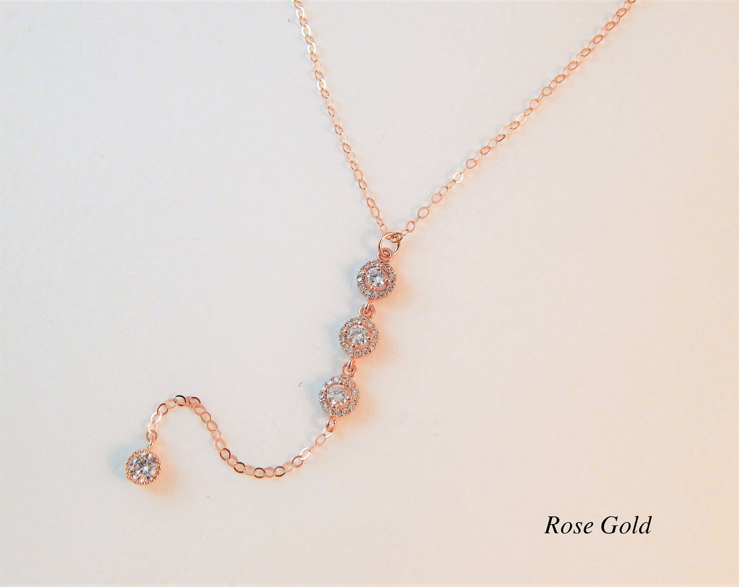 Rose gold wedding necklace with 3 large cubic zirconia diamonds connected in a lariat design on a plain white background.