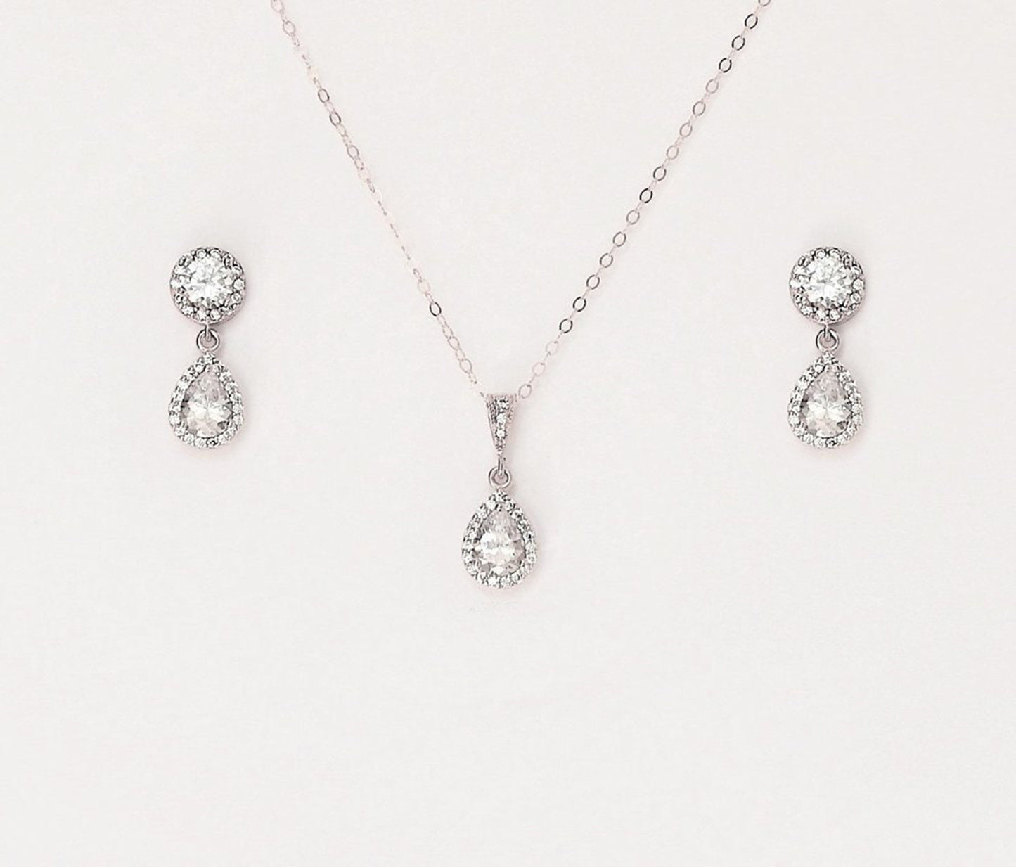 Matching silver necklace and earring set with paved teardrop cubic zirconia on a blank background.