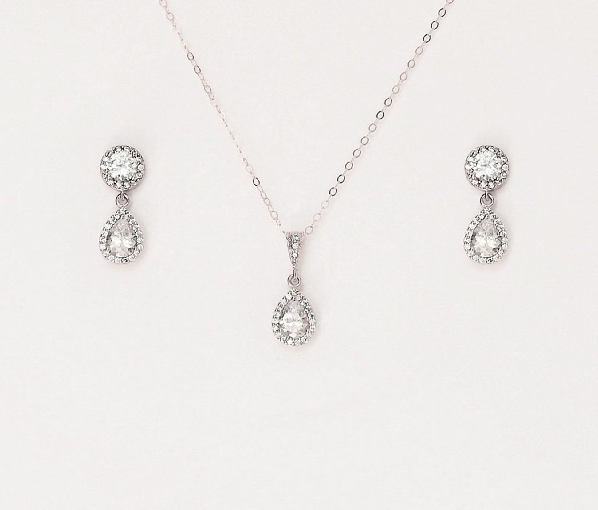Matching silver necklace and earring set with paved teardrop cubic zirconia on a blank background.