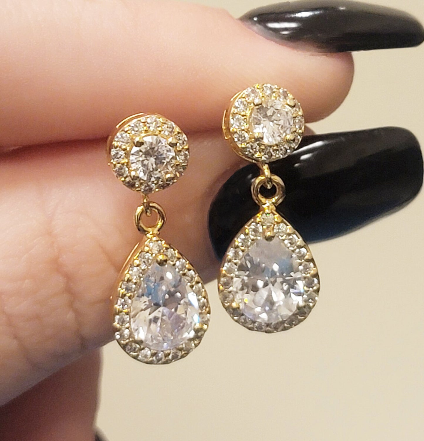 Gold filled special event prom and wedding earrings with many cubic zirconias and large teardrop diamond and held between woman's thumb and forefinger with black manicure.