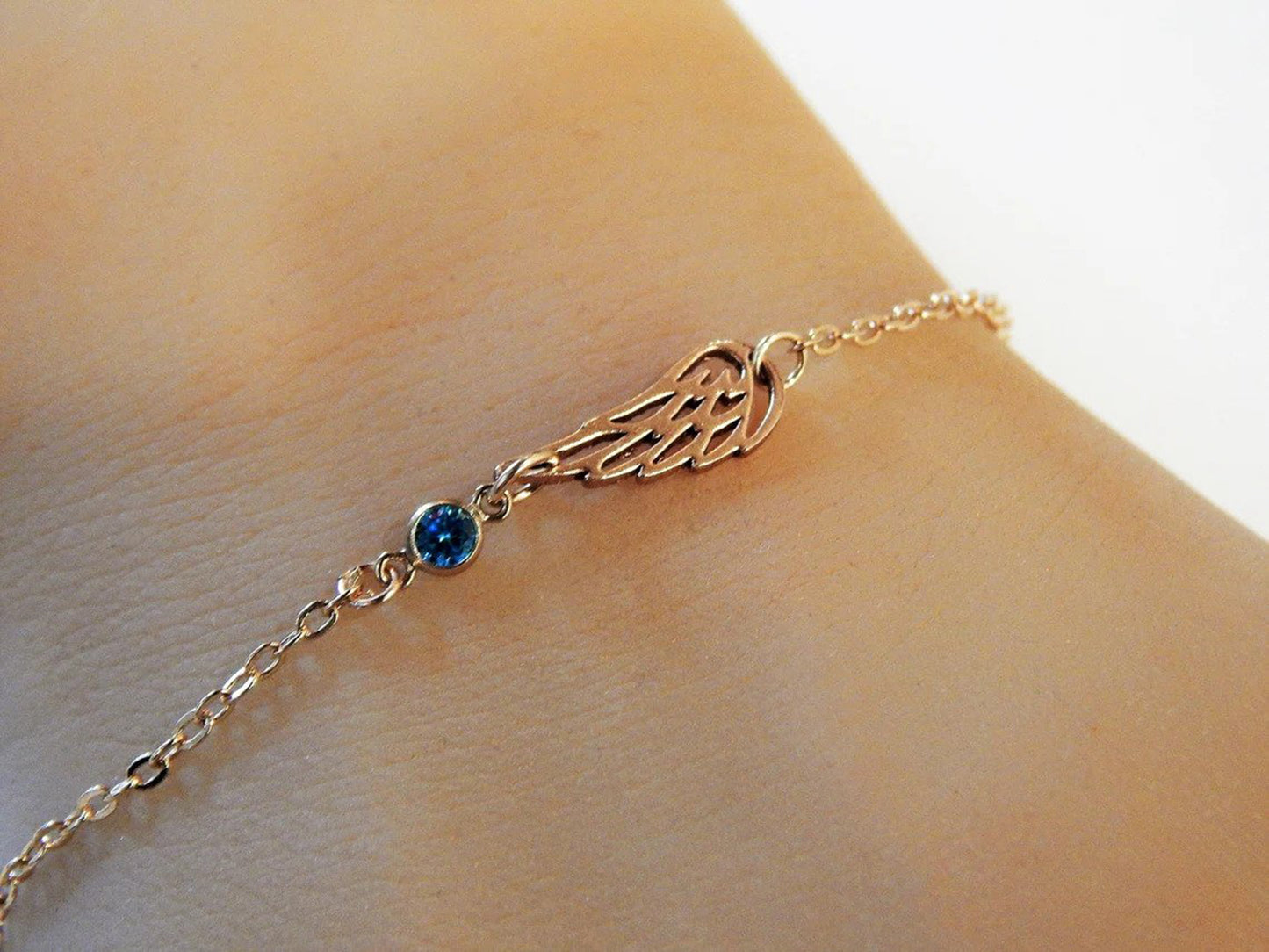 Guardian angel wing charm bracelet with personalized september birthstone option in gold filled chain is worn on a model for Gilded Sapphire's custom jewelry.