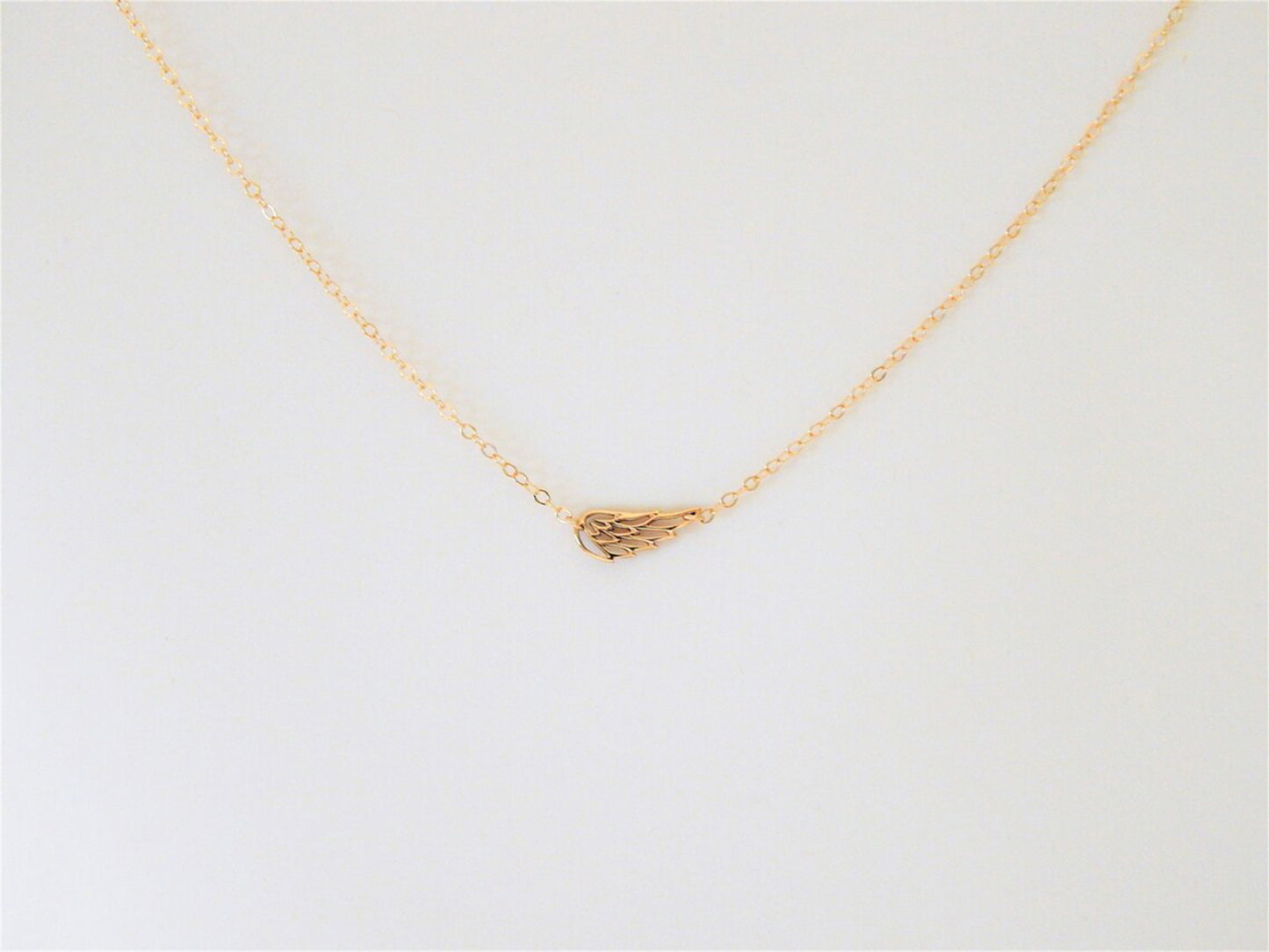 Wing charm on a simple dainty gold filled necklace chain is displayed against a plain white background to showcase the qualities of this sentimental or religious jewelry gift.
