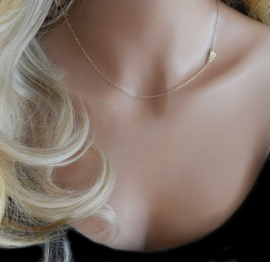 Gold filled necklace choker with guardian angel wing charm placed off center for dainty custom jewelry is worn on a mannequin torso with blonde wavy hair to display Gilded Sapphire's custom handmade jewelry.