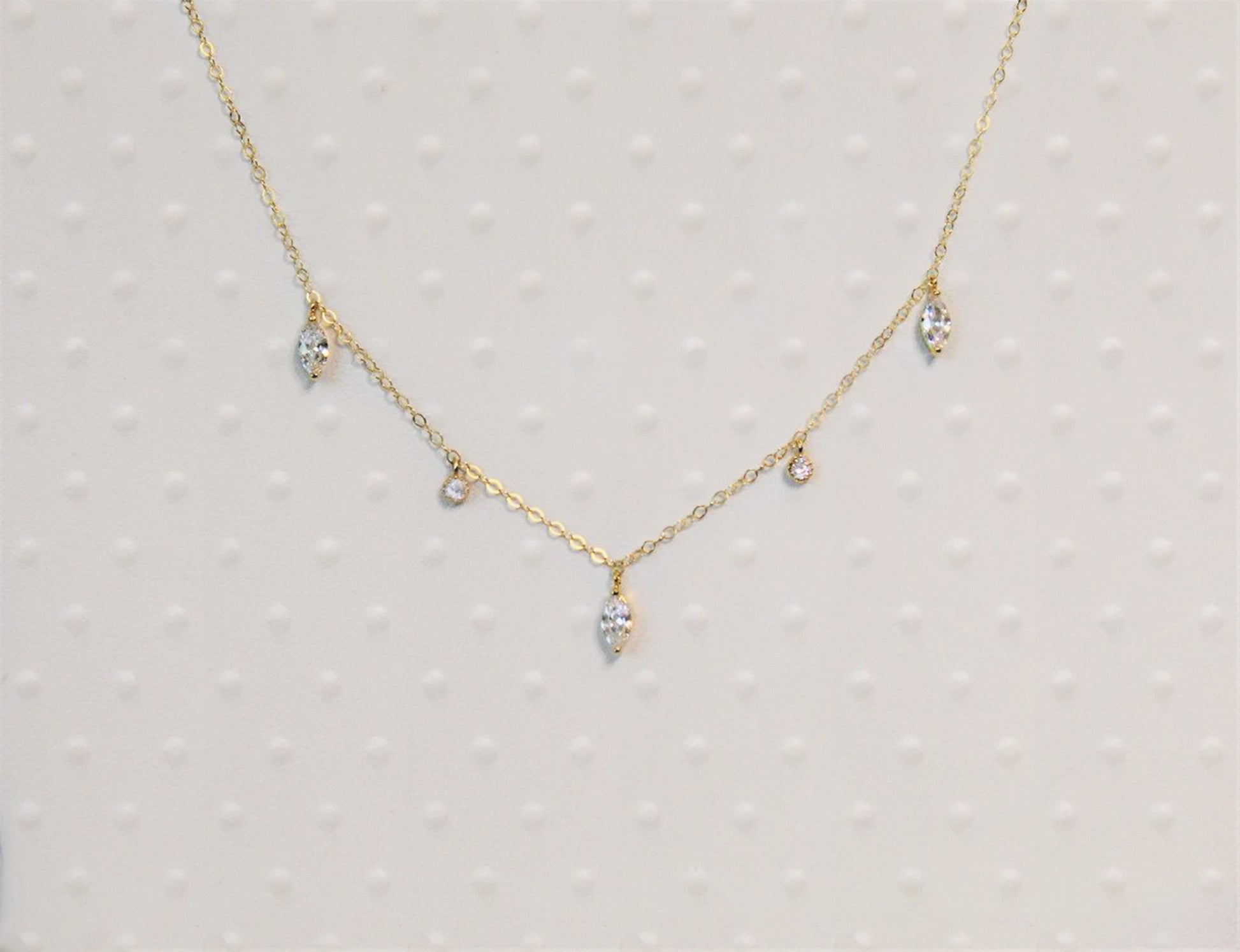 Gold filled cable chain necklace with marquise cut diamonds and round cut diamonds is shown against a textured white background.
