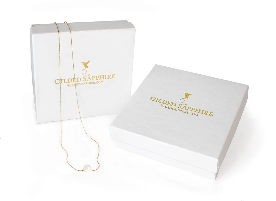 White jewelry gift boxes with a custom logo that has been foil stamped on the top of the boxes are displayed against a bright white bakground to show the packaging by custom jewelry store gilded Sapphire.