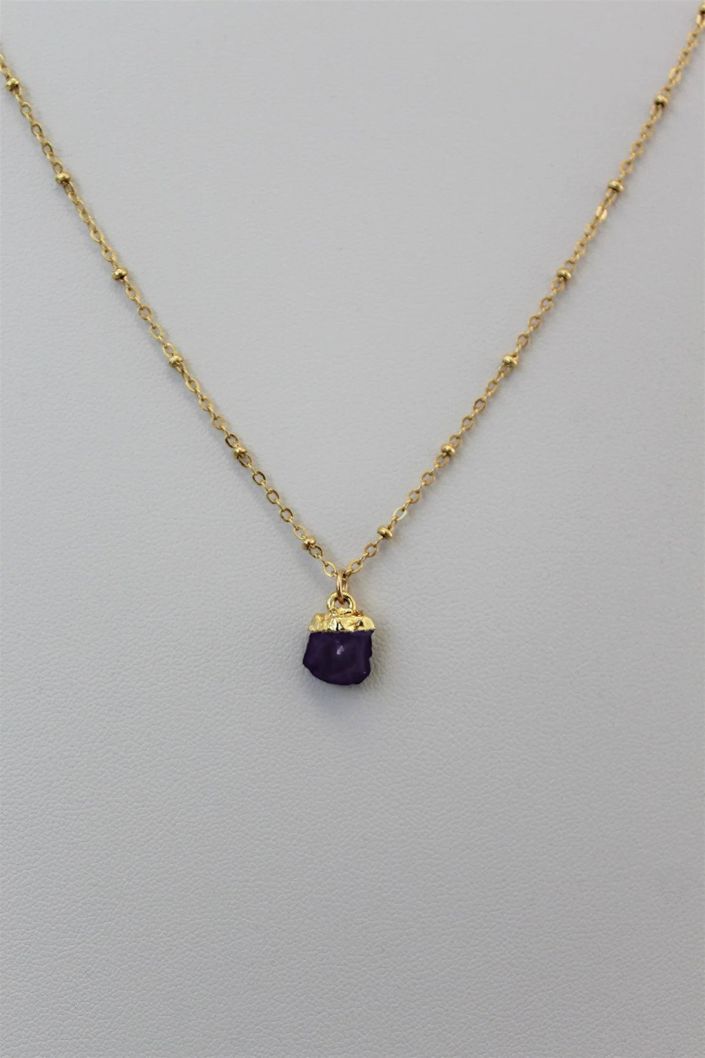Gold filled satellite chain necklace with an electroplated natural amethyst crystal birthstone pendant displayed against a plain white textured background to showcase custom jewelry by Gilded Sapphire. 