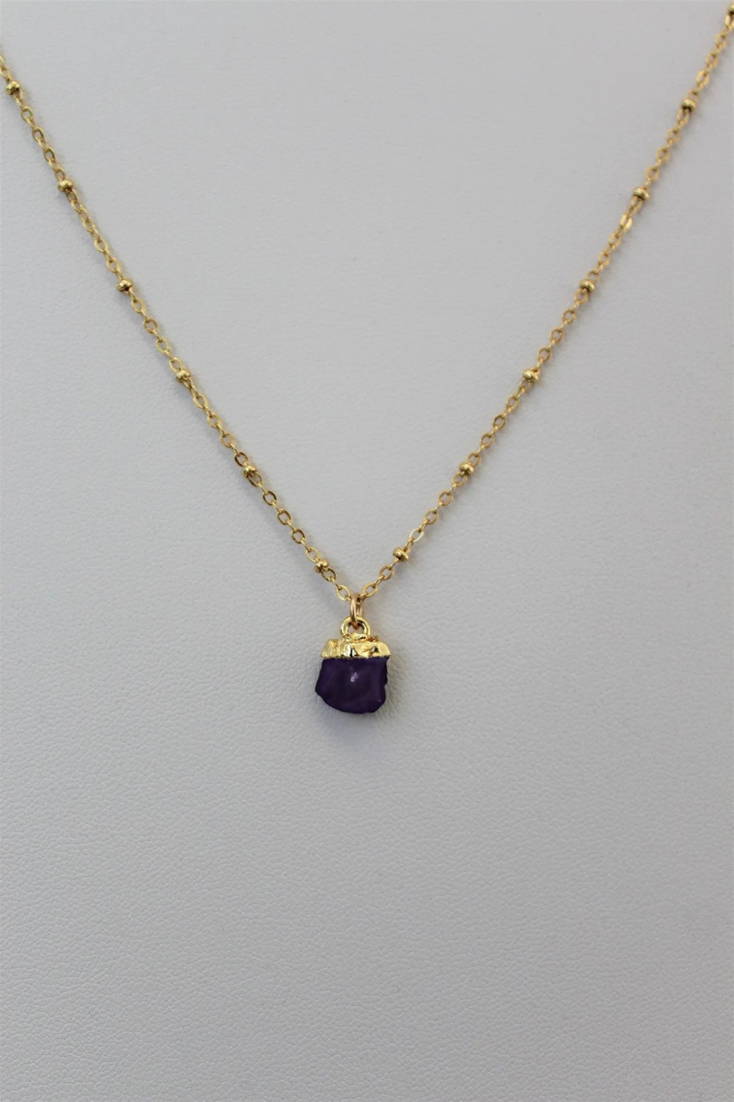 Gold filled satellite chain necklace with an electroplated natural amethyst crystal birthstone pendant displayed against a plain white textured background to showcase custom jewelry by Gilded Sapphire.
