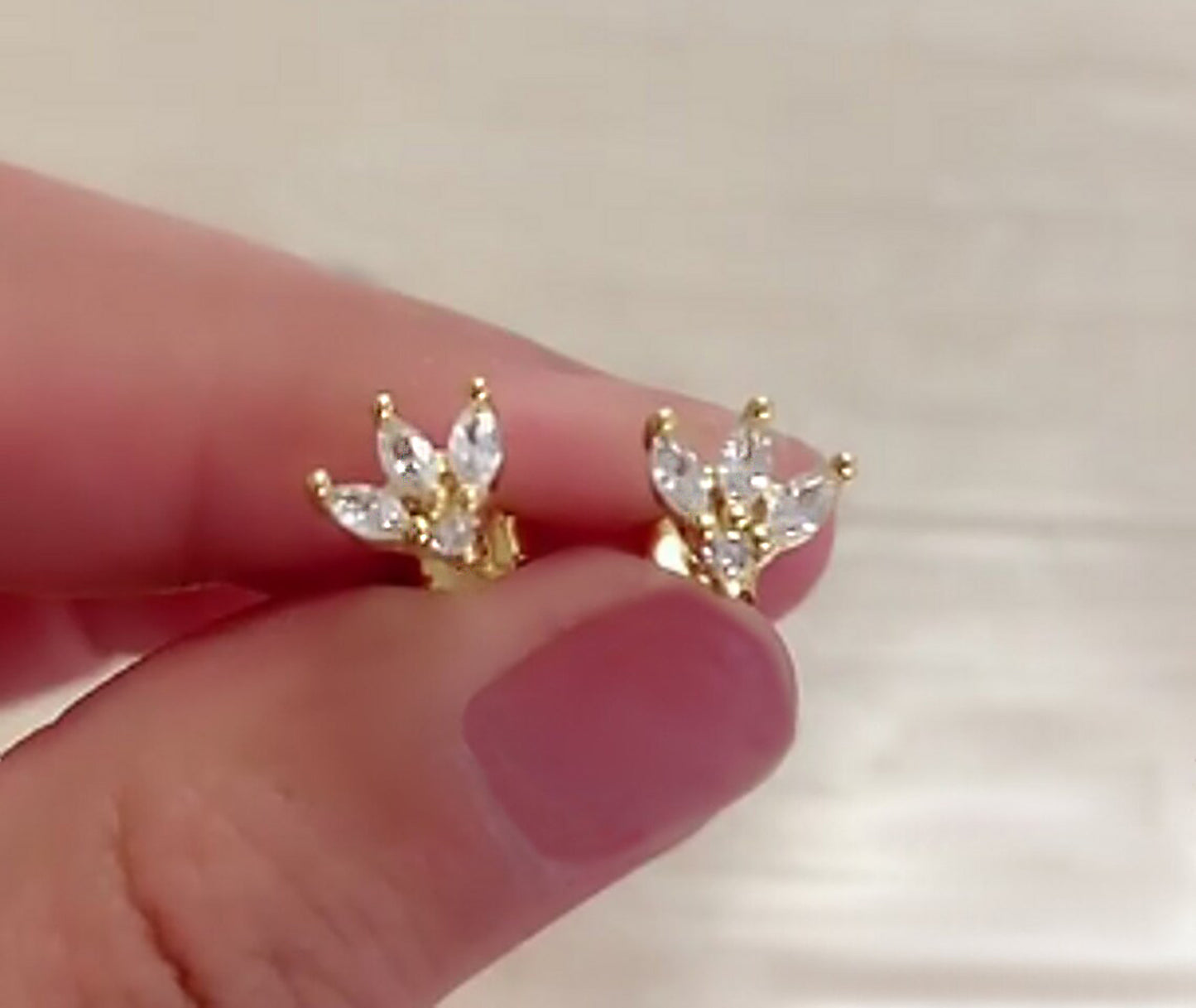 A pair of gold cz earrings held between two manicured fingers to display the features of the earrings.