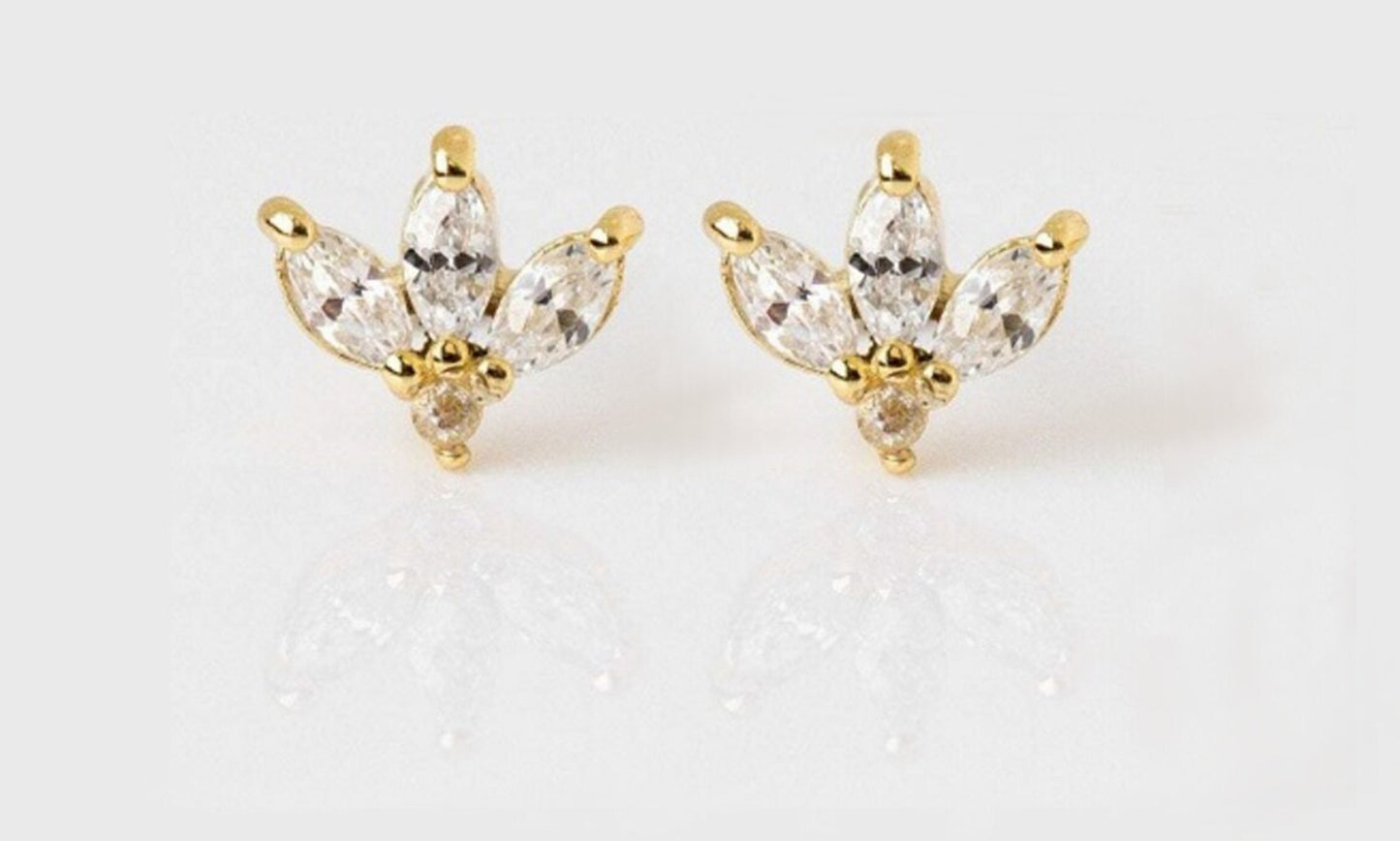 Close up view of a pair of diamond stud earrings with a marquise cut shape set in a gold setting on a white blank surface.