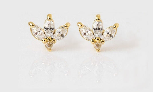 Close up view of a pair of diamond stud earrings with a marquise cut shape set in a gold setting on a white blank surface.