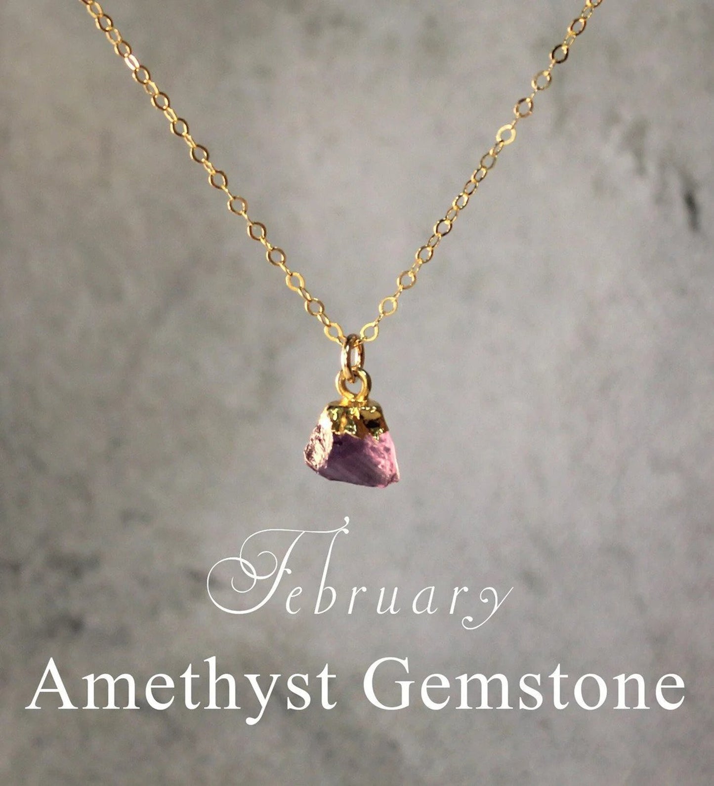 Natural amethyst crystal with an electroplated gold top creates a gemstone pendant that hangs from a gold filled necklace chain displayed against a blurry gray background.