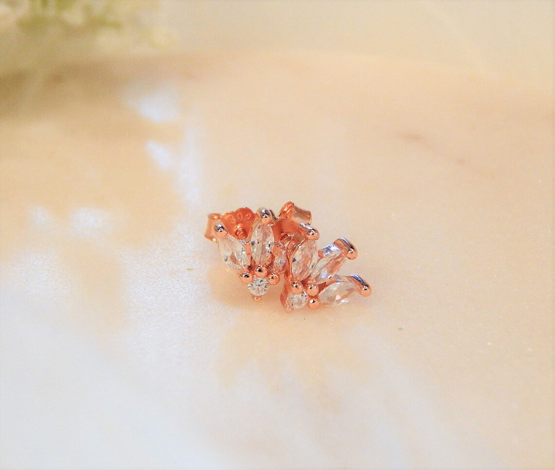 Rose gold diamond earrings are laying on a simple blurry background.