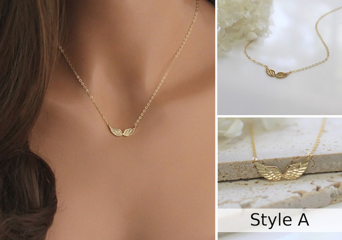 Double Angel Wing Necklace in Gold filled finish is displayed on a manneuin torso, laying on a marble surface, and resting against natural stone tiles..