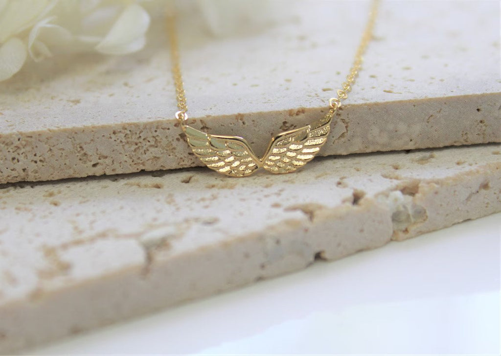 double angel wing custom jewelry charm is displayed against a natural stone tile.