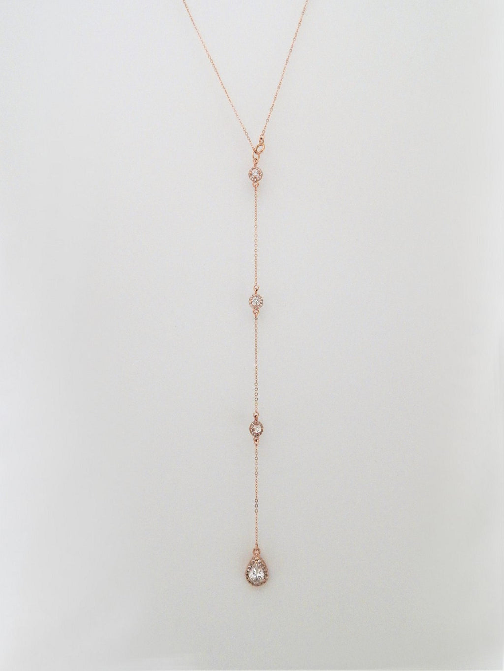 Rose gold backdrop necklace with 3 round diamond cubic zirconias and one large teardop cz on a plain white background.