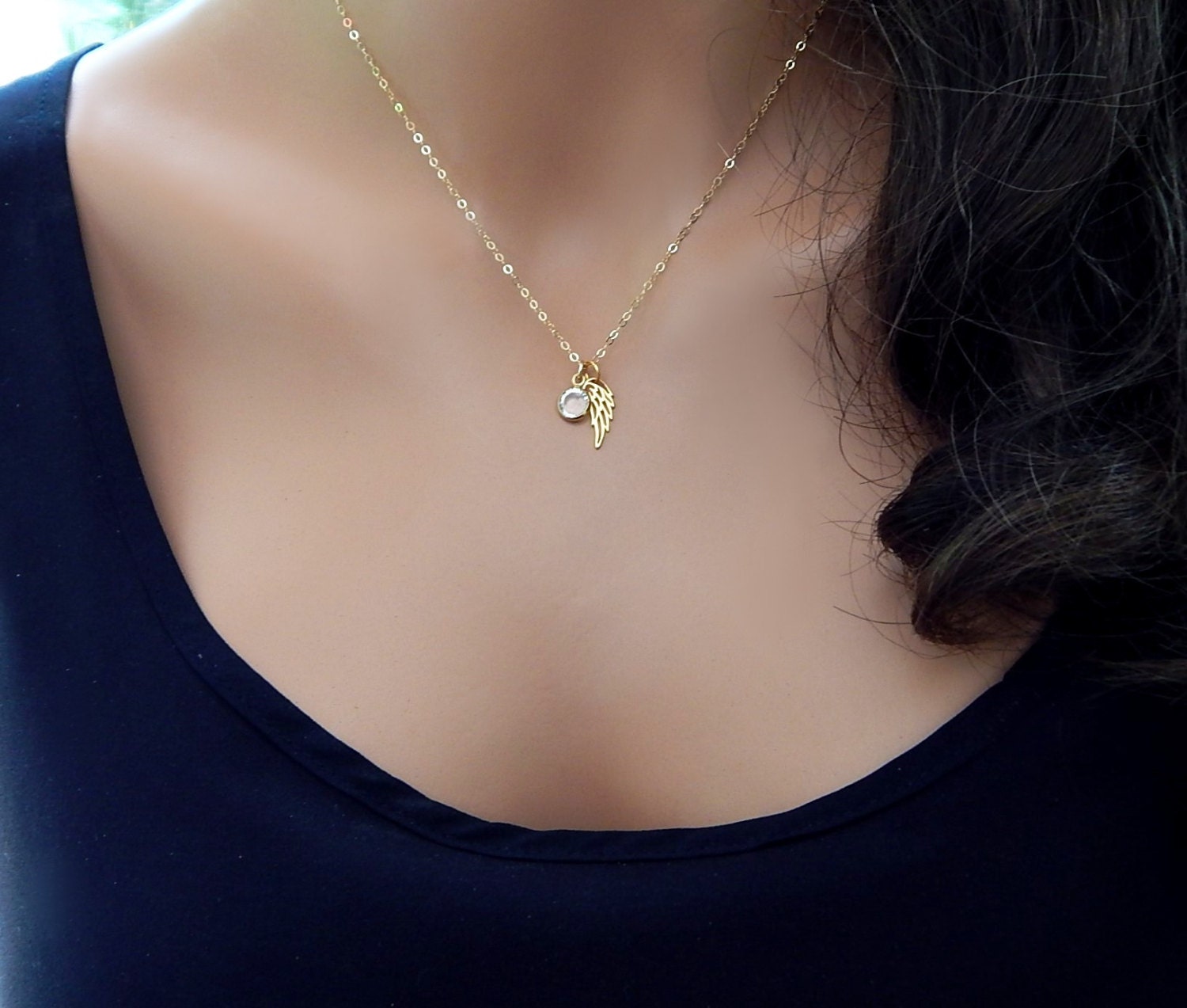 Gold memorial necklace with an angel wing and birthstone on a mannequin torso.