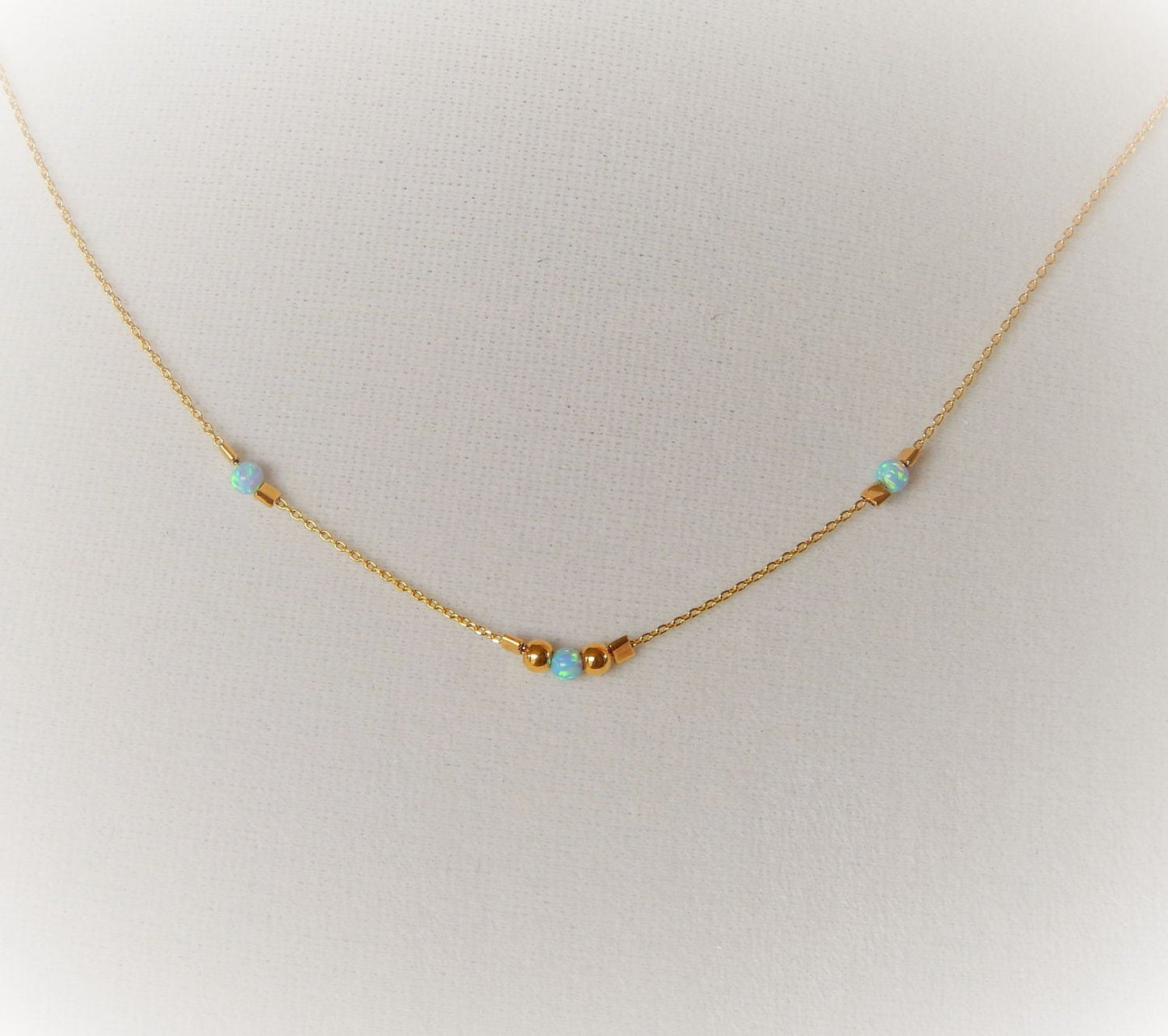 Gold choker with blue opals and gold beads on a blank textured background.