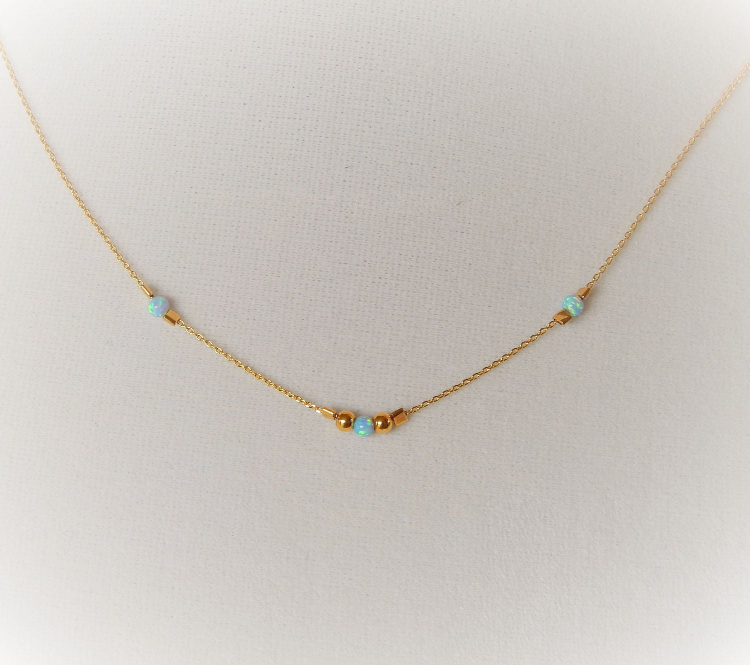 Gold choker with blue opals and gold beads on a blank textured background.