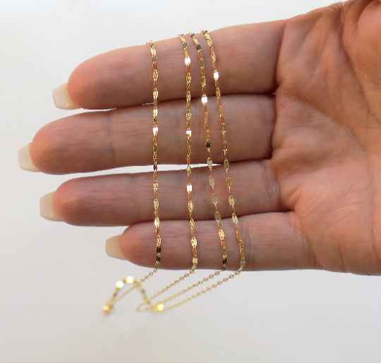 Woman's hand holding a gold sequin necklace chain on her fingers.