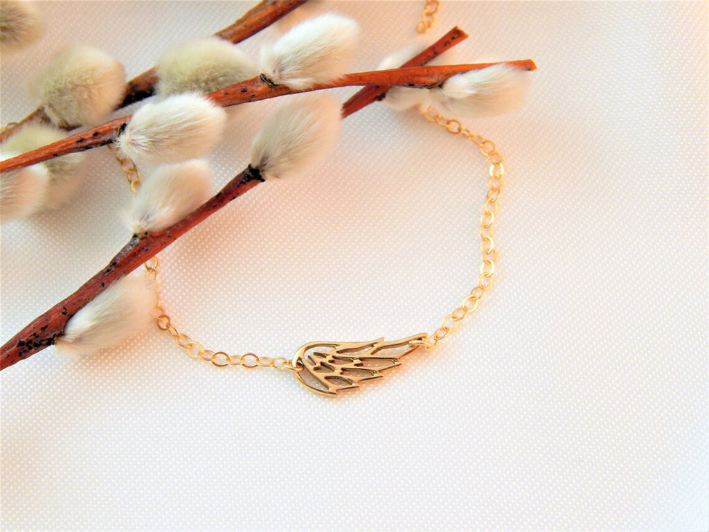 Gold filled necklace chain with guardian angel wing charm creates a dainty memorial necklace that makes a great layering choker or gift for a lost loved one is displayed on a white textured background with decorative foliage.
