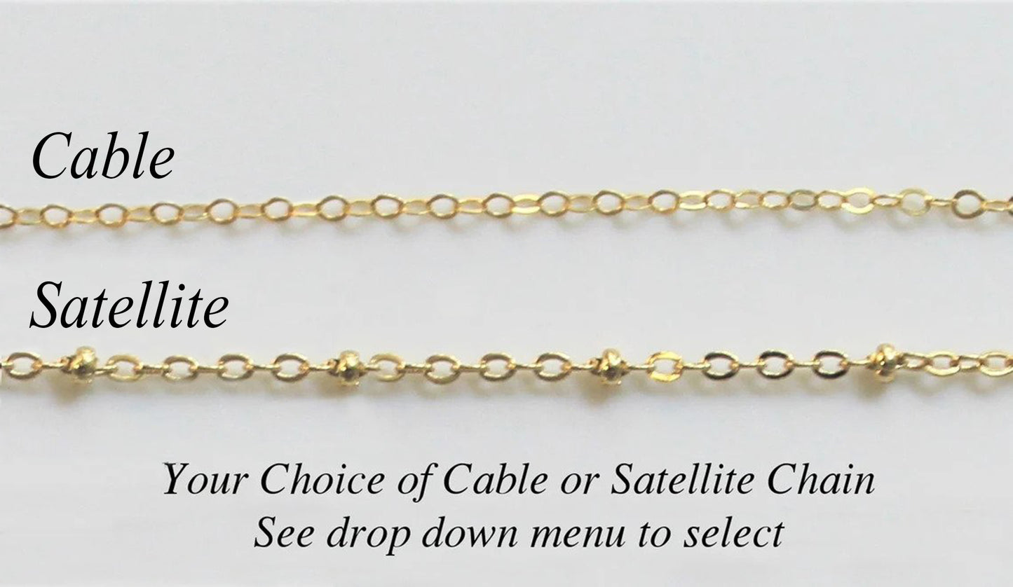 Two different gold filled necklace chain options available by custom jewerly store Gilded Sapphire with cable chain and satellite chain laying on a plain gray surface.