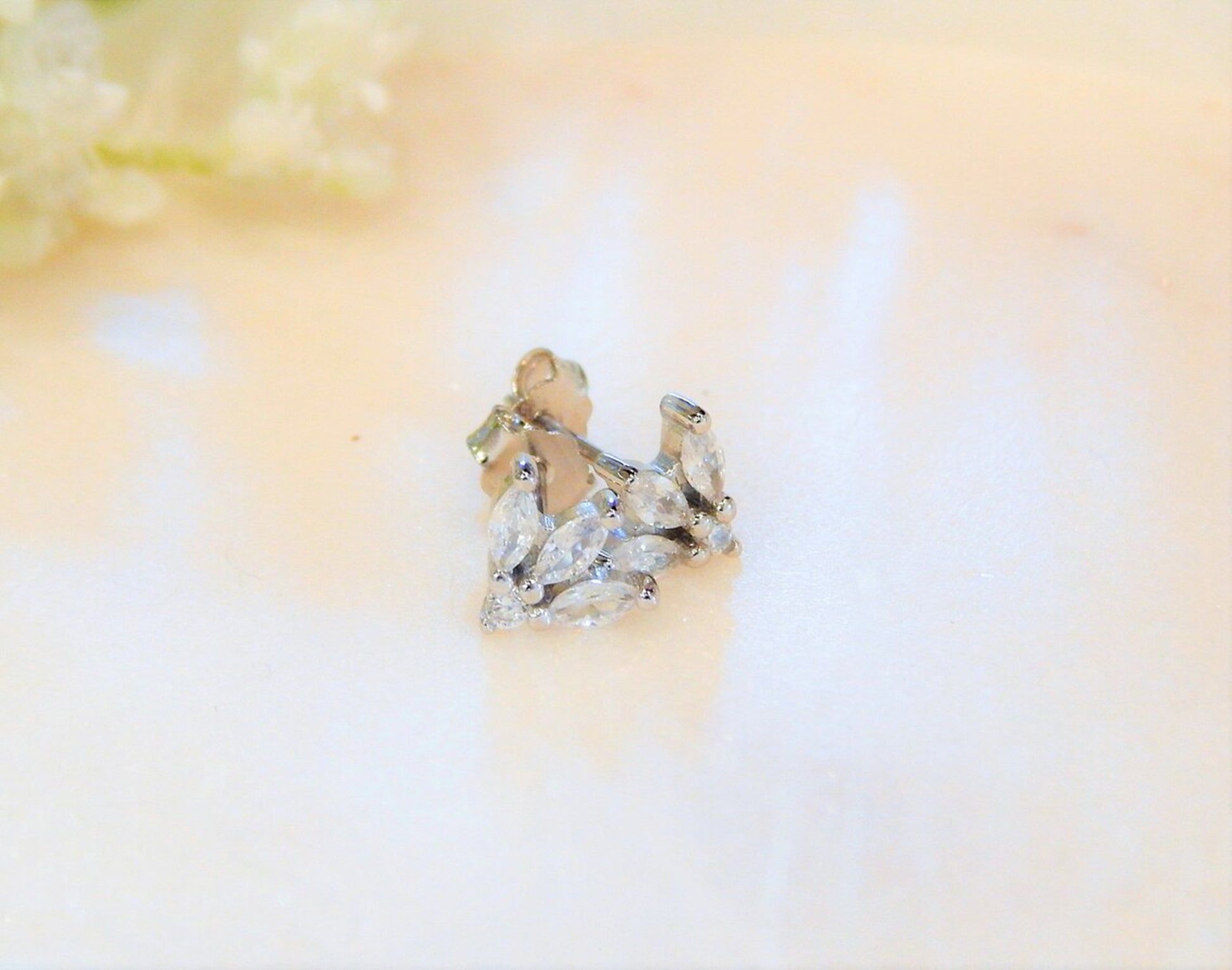 Sterling silver and hypoallergenic earring studs with marquise shaped diamonds are on a light and blurred background.